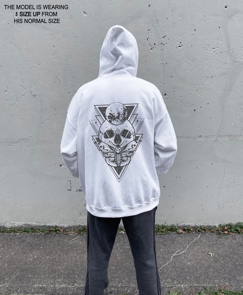 May include: White hooded sweatshirt with a black and white graphic print of a skull with a moth and a crescent moon inside a triangle on the back.