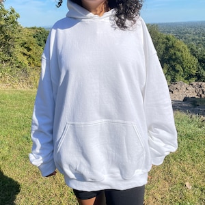 May include: A white oversized hoodie with a kangaroo pocket. The hoodie is made of a soft, comfortable fabric and has a relaxed fit.