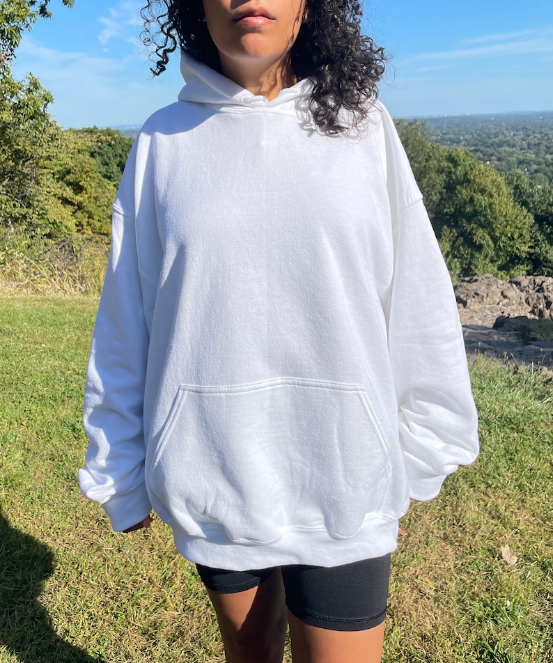 May include: A white oversized hoodie with a kangaroo pocket. The hoodie is made of a soft, comfortable fabric and has a relaxed fit.