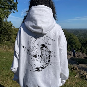 May include: White hooded sweatshirt with a black and white graphic print of two koi fish swimming. The model is wearing the sweatshirt two sizes up from her normal size.