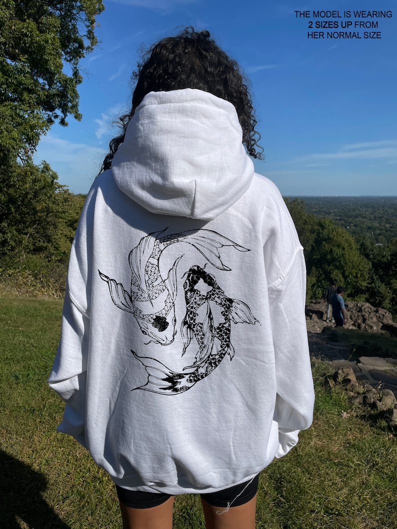 May include: White hooded sweatshirt with a black and white graphic print of two koi fish swimming. The model is wearing the sweatshirt two sizes up from her normal size.
