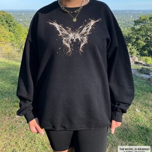 Pode incluir: Camisola de moletom preta com estampa de borboleta marrom. A modelo est&aacute; usando a camisola dois tamanhos maiores do que seu tamanho normal.