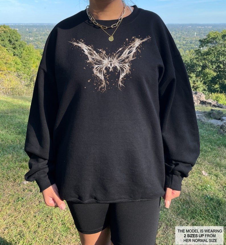Pode incluir: Camisola de moletom preta com estampa de borboleta marrom. A modelo est&aacute; usando a camisola dois tamanhos maiores do que seu tamanho normal.