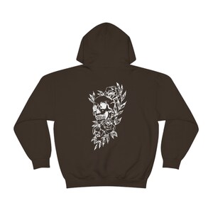 Puede incluir: Una sudadera con capucha marr&oacute;n oscuro con un estampado blanco de una calavera rodeada de flores.