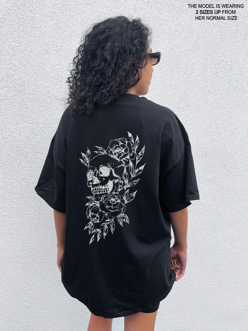 May include: Black oversized t-shirt with a white graphic print of a skull with flowers. The model is wearing the shirt two sizes up from her normal size.