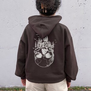 May include: A brown hoodie with a white graphic of a skull with trees growing out of it on the back. The skull is surrounded by a globe.