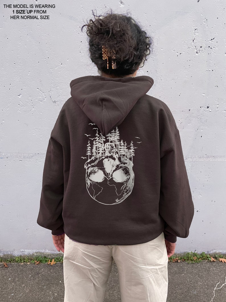 May include: A brown hoodie with a white graphic of a skull with trees growing out of it on the back. The skull is surrounded by a globe.