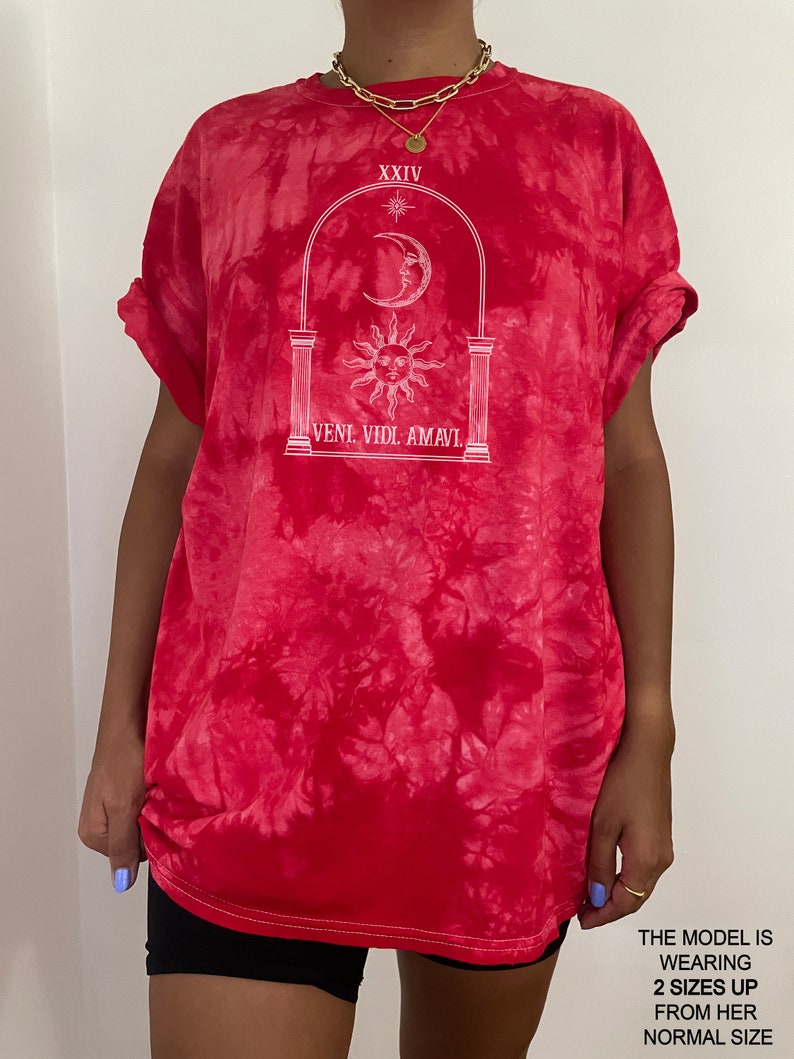 May include: Red tie-dye t-shirt with a white graphic of an archway with a sun and moon inside. The text "XXIV" and "VENI. VIDI. AMAVI." are printed on the shirt.