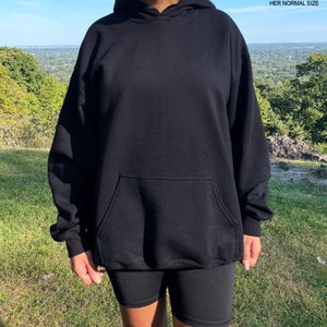May include: Black oversized hoodie with a kangaroo pocket. The model is wearing the hoodie two sizes up from her normal size.