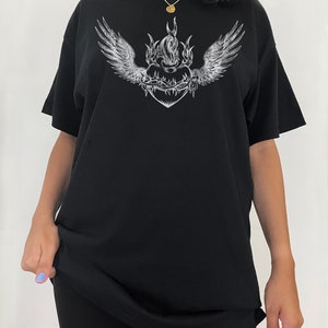 May include: Black oversized t-shirt featuring a graphic print of a flaming heart with wings and barbed wire. The model is wearing the shirt two sizes up from her usual size.
