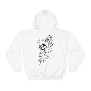 Puede incluir: Sudadera con capucha blanca con un estampado gr&aacute;fico en blanco y negro de una calavera rodeada de flores.