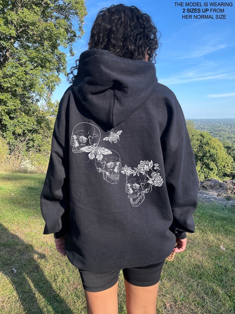 May include: Black hooded sweatshirt with a white graphic of three skulls with flowers and a butterfly on the back.