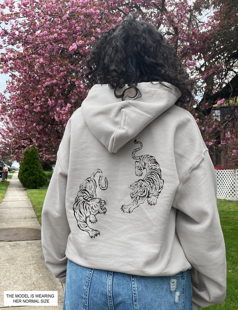 May include: A light gray hoodie with a black tiger graphic on the back. The hoodie has a drawstring hood and a kangaroo pocket.