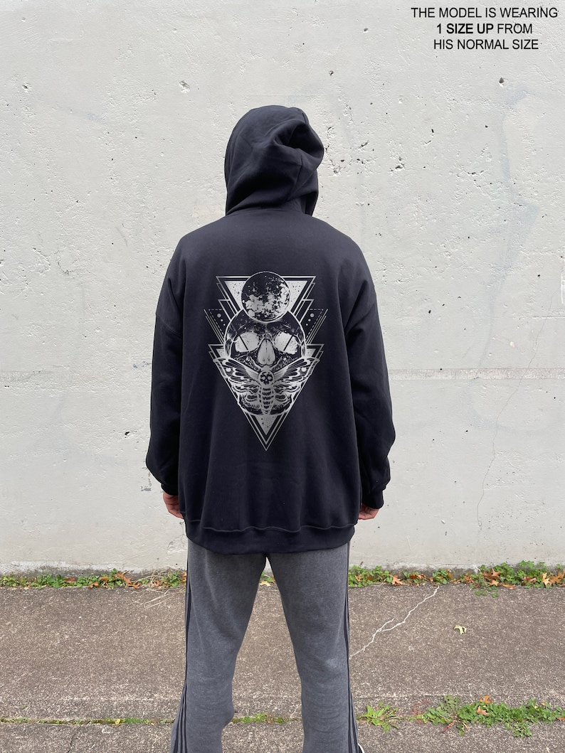 May include: Black hooded sweatshirt with a graphic print of a skull with a moth and a crescent moon. The graphic is in a geometric triangle design.