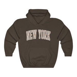 May include: A brown hooded sweatshirt with the text "NEW YORK" in a beige color on the front.