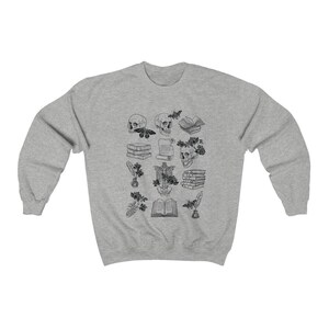 May include: A gray sweatshirt with a black and white illustration of skulls, books, flowers, and other objects. The illustration is centered on the sweatshirt.