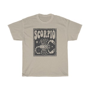 May include: A beige t-shirt with a black and white graphic of a scorpion with the word "SCORPIO" in a retro font.