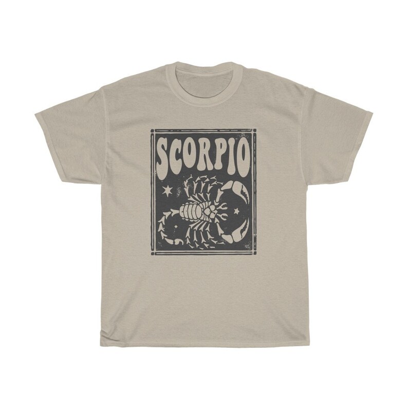 May include: A beige t-shirt with a black and white graphic of a scorpion with the word "SCORPIO" in a retro font.