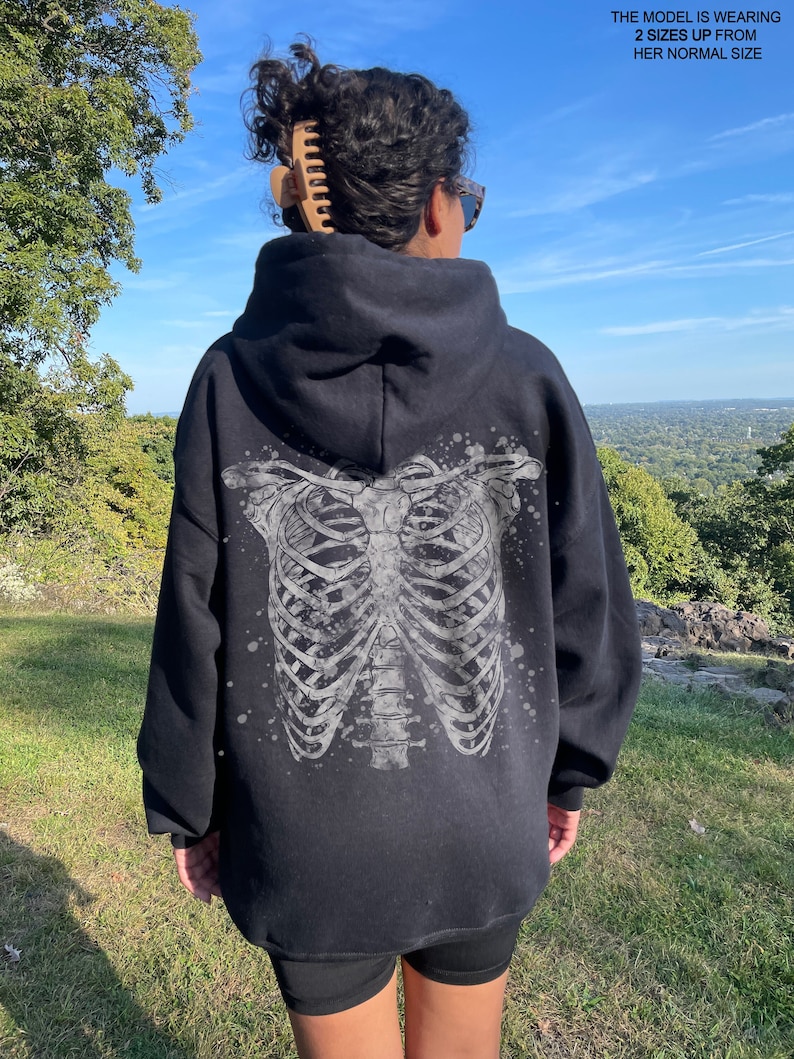 May include: Black hooded sweatshirt with a white skeleton ribcage graphic on the back. The model is wearing the sweatshirt two sizes up from her normal size.