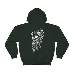 Puede incluir: Una sudadera con capucha verde oscuro con un estampado blanco de una calavera rodeada de flores.