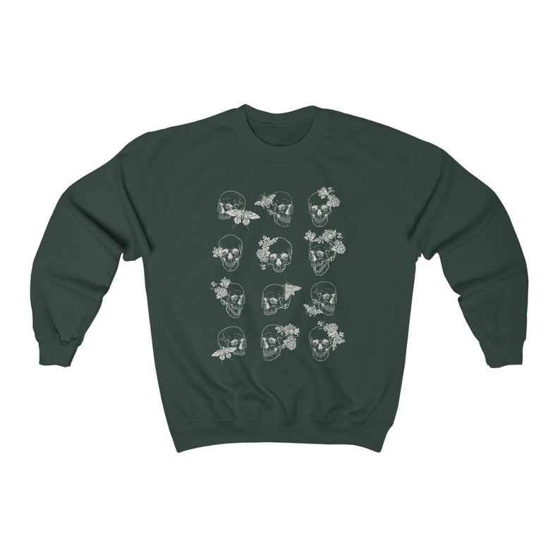 K&ouml;nnte beinhalten: Ein dunkelgr&uuml;ner Pullover mit einem wei&szlig;en Druck von mehreren Sch&auml;deln mit floralen und Schmetterlings-Akzenten.