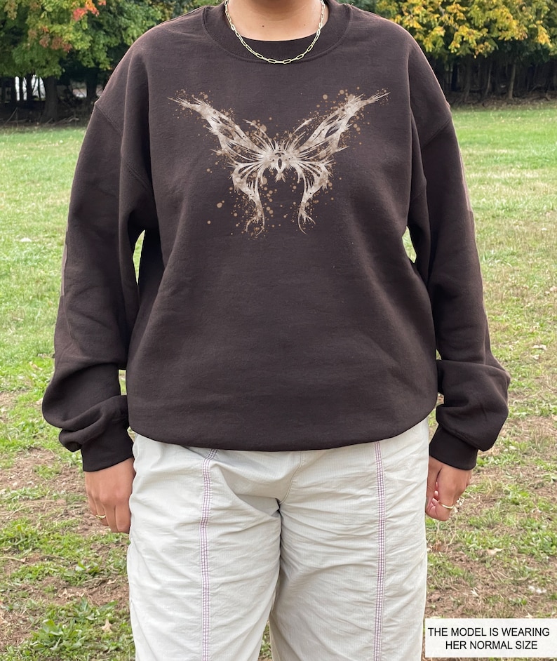 Pode incluir: Uma camisa de moletom marrom com uma estampa de borboleta branca. A borboleta tem um efeito de tinta salpicada. A modelo est&aacute; usando seu tamanho normal.