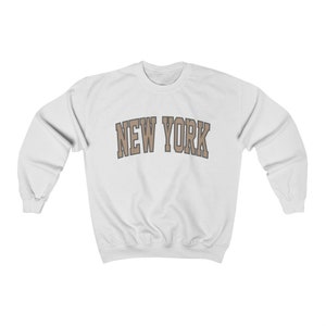 May include: White sweatshirt with a brown "NEW YORK" graphic printed on the front.