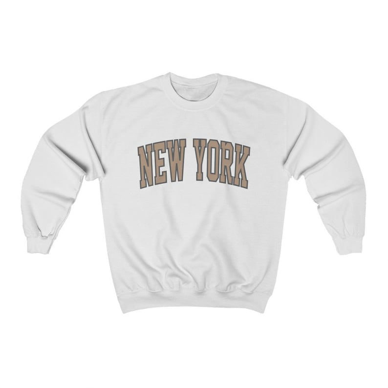 May include: White sweatshirt with a brown "NEW YORK" graphic printed on the front.