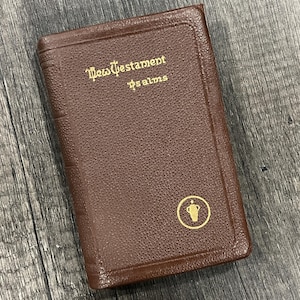 May include: A brown leather-bound book with gold lettering that reads "New Testament Psalms." A gold emblem is on the lower right corner. The book has a textured surface.