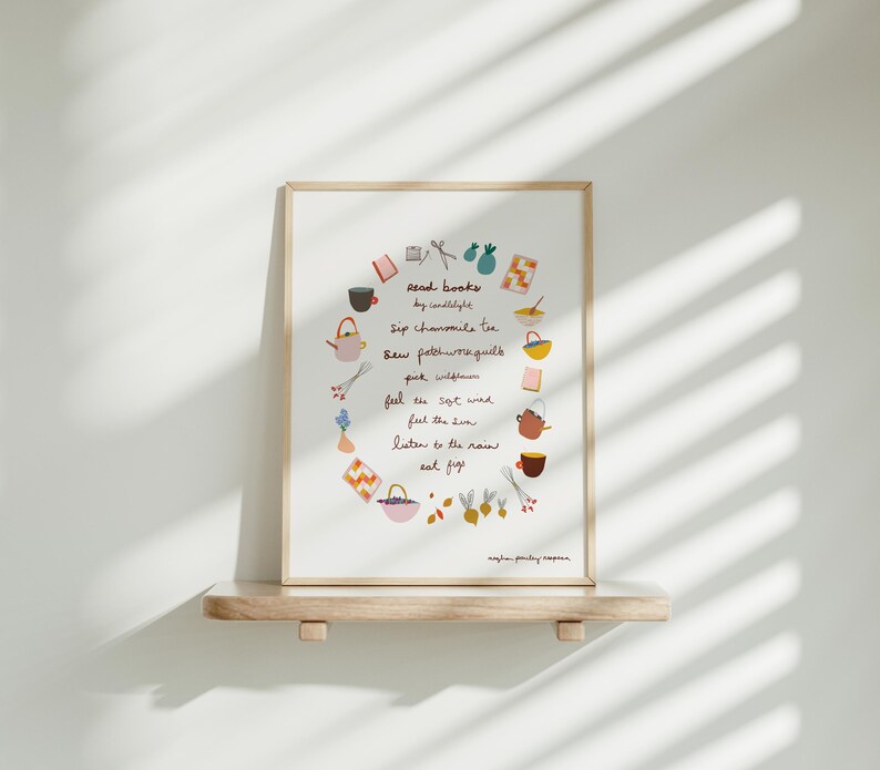 May include: A framed print with a light wood frame. The print features a circular arrangement of illustrated objects and handwritten text, including phrases like "Read books by candlelight" and "Sip chamomile tea."