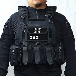 Puede incluir: Un chaleco táctico negro con múltiples bolsillos y correas. El chaleco tiene un parche con la bandera del Reino Unido y las letras "SAS" en él.