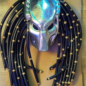 May include: A silver Predator mask with black dreadlocks. The dreadlocks have gold accents.