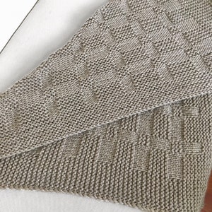 Op de afbeelding: Een beige gebreide deken met een textuurpatroon. De deken is dubbelgevouwen, waardoor het patroon aan beide kanten zichtbaar is.