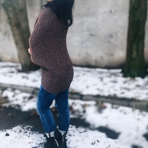 May include: A woman wearing a brown knitted cardigan, blue jeans, and black boots. She is standing in a snowy outdoor setting.