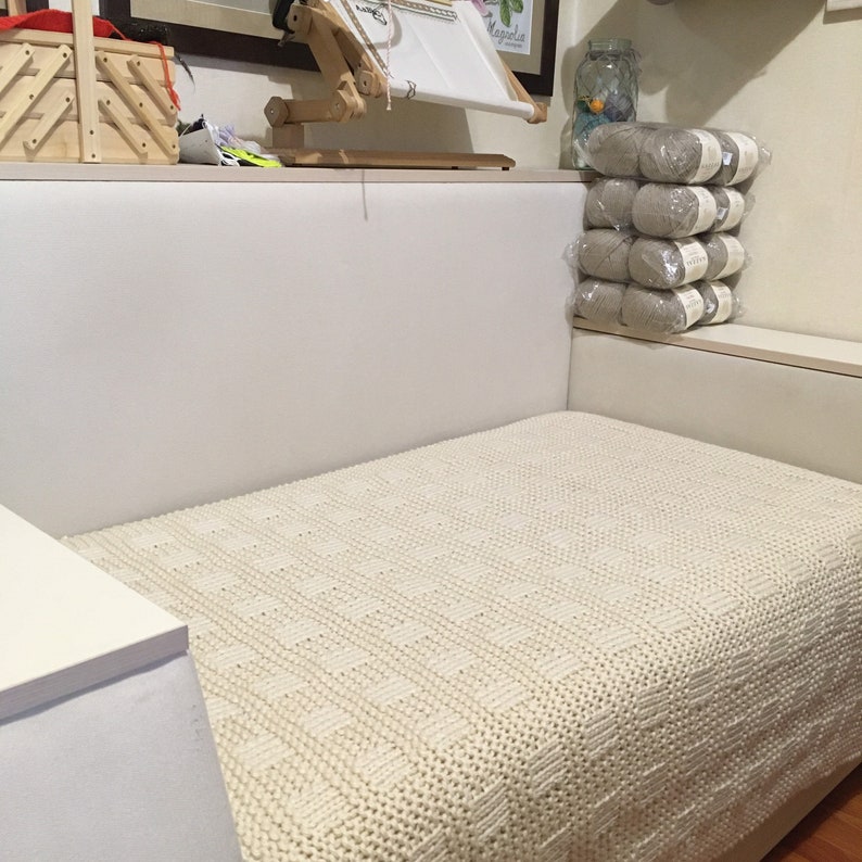 May include: A white knitted throw blanket with a textured pattern is draped over a white couch.