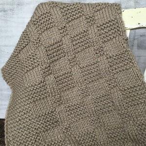 Puede incluir: Una manta de punto marrón con un patrón cuadrado.