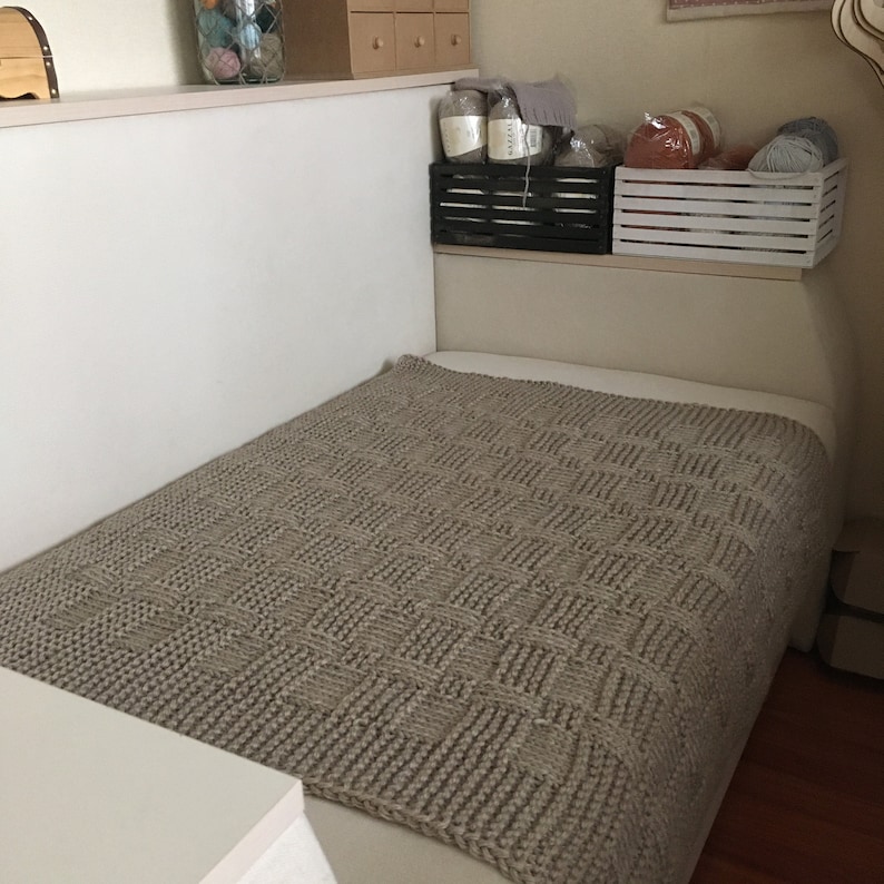 Op de afbeelding: Een bruin gebreid deken met een textuurpatroon ligt op een bed.