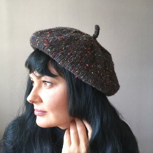 Puede incluir: Un gorro marrón con motas multicolores. El gorro es de punto y tiene un pequeño pompón en la parte superior.