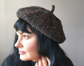 May include: A brown beret with multicolored flecks. The beret is knitted and has a small pompom on top.