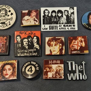 以下が含まれることがあります： AC/DC、The Kinks、Madonnaなど、ヴィンテージのバンドピンとバッジのコレクション。ピンには、バンドのロゴ、アルバムアート、ツアーの日付など、さまざまなデザインが施されています。バッジはさまざまな形とサイズです。