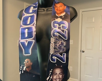 May include: A blue and black graduation sash with the name "Cody" and the year "2023" printed on it. The sash also features a black panther logo and a photo of a graduate.
