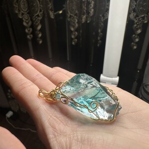 May include: A gold wire wrapped pendant featuring a large, clear, light blue and green crystal.