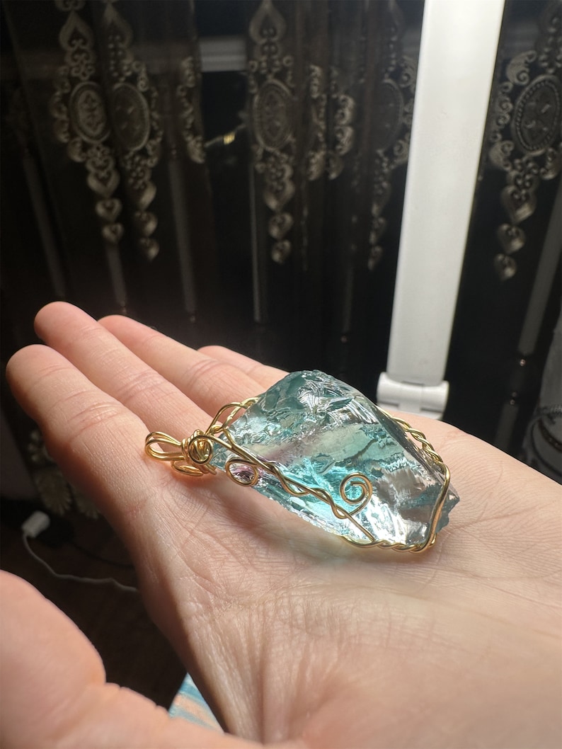 May include: A gold wire wrapped pendant featuring a large, clear, light blue and green crystal.