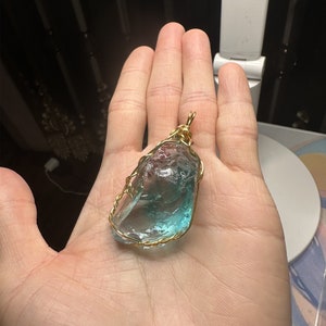 May include: A blue and green crystal pendant wrapped in gold wire. The pendant is a natural, irregular shape and is suspended from a gold wire loop.
