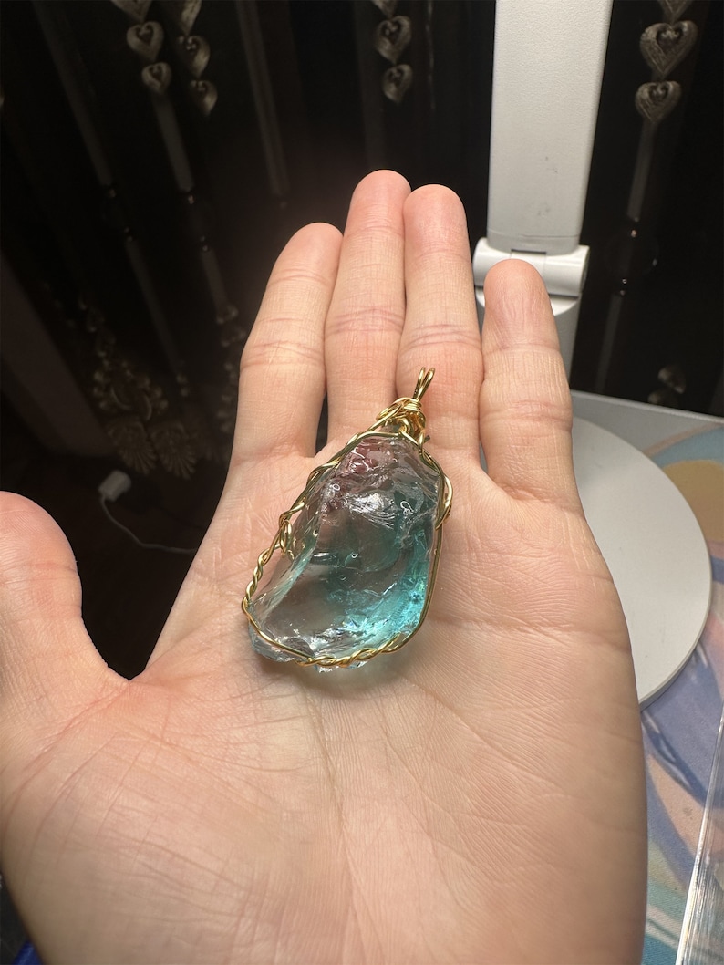 May include: A blue and green crystal pendant wrapped in gold wire. The pendant is a natural, irregular shape and is suspended from a gold wire loop.