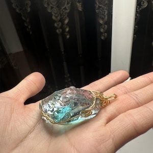 May include: A blue and green glass pendant wrapped in gold wire. The pendant is shaped like a rough, natural stone.