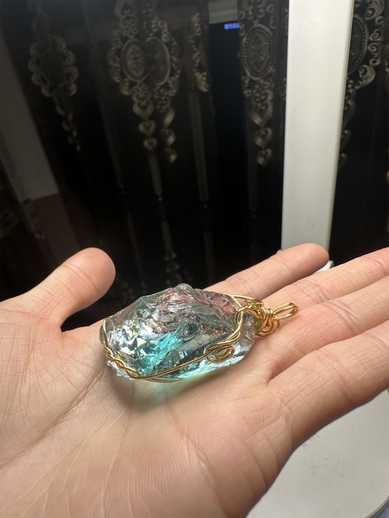 May include: A blue and green glass pendant wrapped in gold wire. The pendant is shaped like a rough, natural stone.