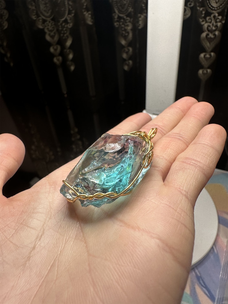 May include: A blue and green glass pendant wrapped in gold wire. The pendant is shaped like a rough, irregular stone.