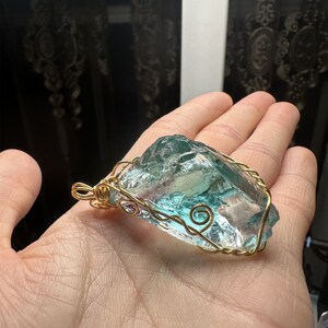May include: A teal blue and clear glass pendant wrapped in gold wire. The pendant is shaped like a large, irregular rock.