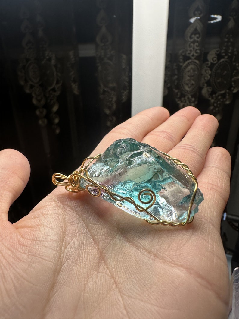 May include: A teal blue and clear glass pendant wrapped in gold wire. The pendant is shaped like a large, irregular rock.